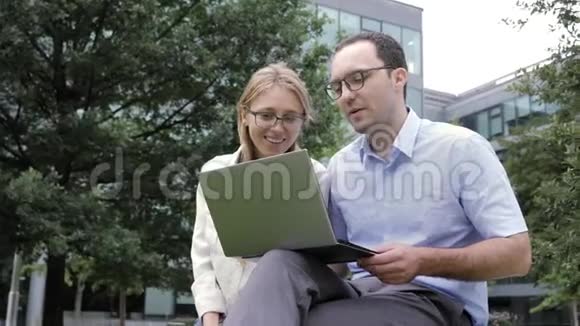 商务朋友在办公楼附近的公园里用笔记本电脑工作视频的预览图