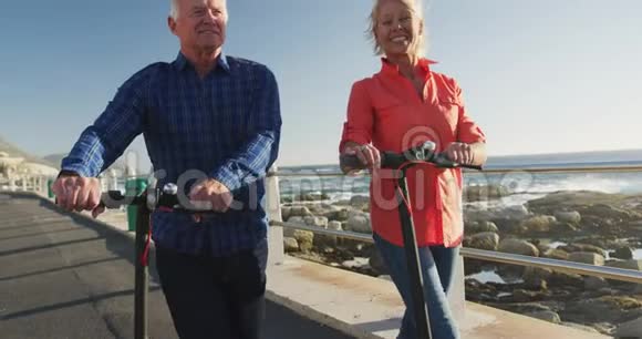 一对老夫妇走在海边的电子滑板车旁边视频的预览图