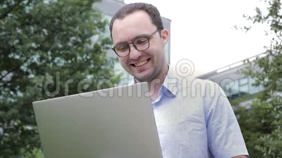 喜剧情感奈德商人带着疯狂的微笑在户外用他的笔记本电脑工作视频的预览图