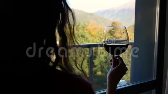 年轻美貌女子的剪影酒杯窗前山景视频的预览图
