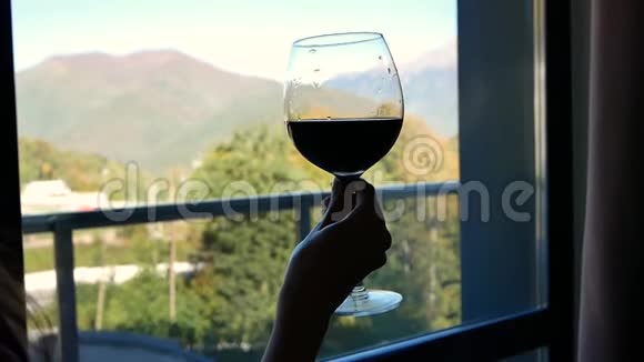 在窗外的背景上用美丽的山景特写女性手中酒杯的轮廓视频的预览图