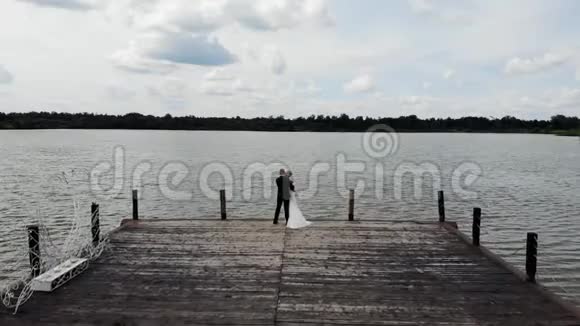 在木墩上拥抱新郎新娘的空中飞行飞越湖面视频的预览图