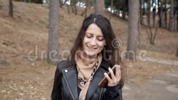 年轻的女人正在穿过公园打电话微笑的女人在打电话她高兴打电话来视频的预览图