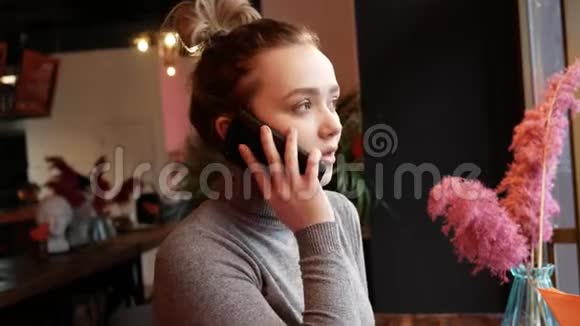 年轻的金发女人在咖啡馆里打电话笑着笑着喝着纸杯里的咖啡视频的预览图