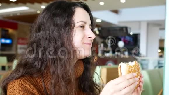 年轻漂亮的微笑着的女人在咖啡馆吃汉堡视频的预览图