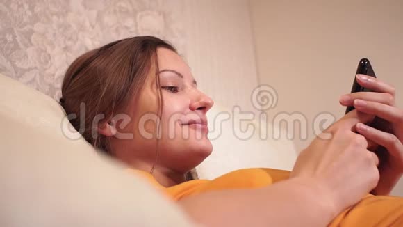年轻女孩特写在家看智能手机用手机躺在床上幸福的家庭画像视频的预览图