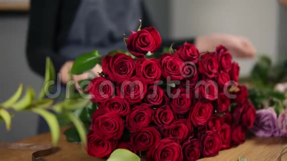 桌子上放着一束完美的红玫瑰采用现代花束的女性花店手的特写镜头视频的预览图