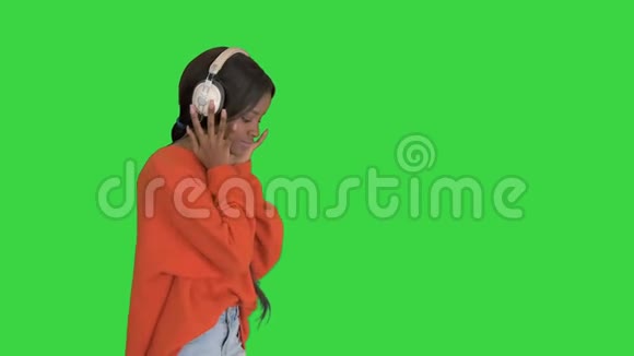 快乐的非洲女人戴着无线耳机在绿色屏幕上听音乐Chroma键视频的预览图