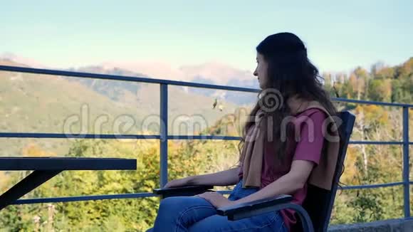 美丽的年轻女子坐在户外咖啡馆的桌旁欣赏美丽的山景视频的预览图