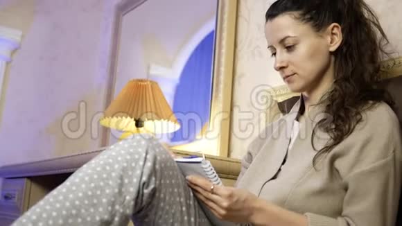美丽的年轻女子在卧室的笔记本上用钢笔写字视频的预览图
