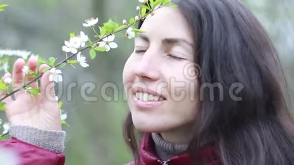 美丽的年轻女子在花园里嗅着一棵开花的树视频的预览图