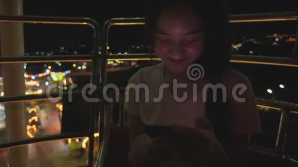 在游乐园乘坐摩天轮时亚洲女孩很兴奋美女享受城市高层的夜间活动嘉年华视频的预览图