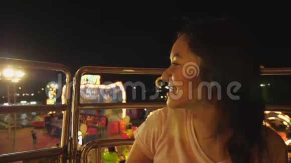 在游乐园乘坐摩天轮时亚洲女孩很兴奋美丽的女人在城市的高景下享受夜间狂欢节的活动视频的预览图