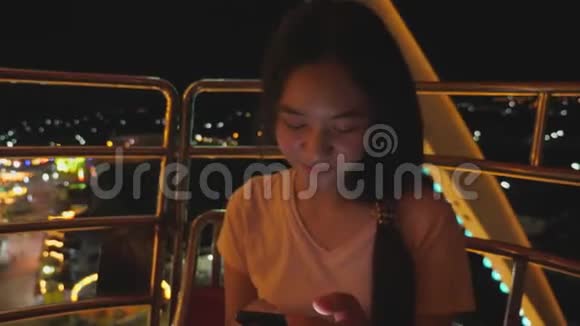 在游乐园乘坐摩天轮时亚洲女孩很兴奋美女享受城市高层的夜间活动嘉年华视频的预览图