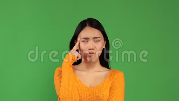 一位亚洲女人在镜头前的绿色背景上将食指放在太阳穴附近视频的预览图