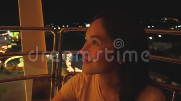 在游乐园乘坐摩天轮时亚洲女孩很兴奋美丽的女人在城市的高景下享受夜间狂欢节的活动视频的预览图