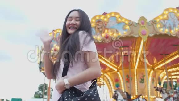 快乐美丽的亚洲女人在游乐园享受旋转木马看着并向相机挥手人民的生活方式和视频的预览图