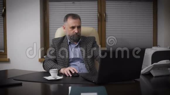 尊敬的绅士头发灰白办公室主任在用笔记本电脑和咖啡视频的预览图