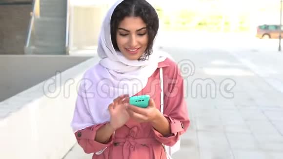 年轻的穆斯林妇女戴着头巾使用她的智能手机视频的预览图