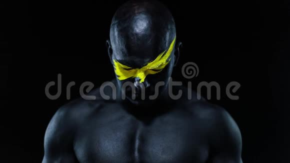 男子健美运动员的特写肖像脸上有黄色的艺术和黑色的身体油漆彩色照片视频的预览图