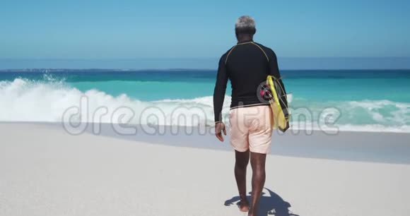 后景老人带着冲浪板在海滩散步视频的预览图