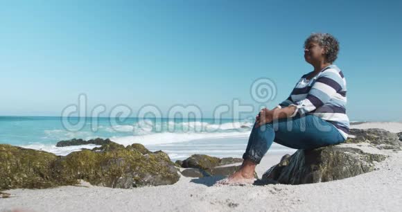从侧面看老妇人坐在海滩上的岩石上视频的预览图