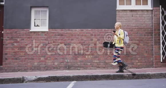 一个混血女人拿着滑板和手机走在街上视频的预览图