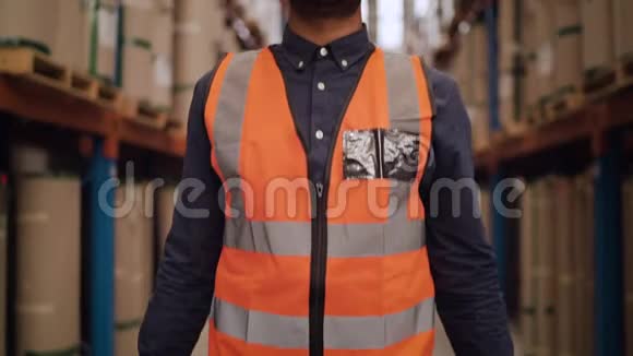 在一个大仓库里一个微笑自信的仓库工人用手臂站立着保护帽子的肖像交叉了起来视频的预览图