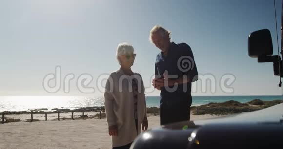 前景老夫妇在海滩上使用智能手机视频的预览图