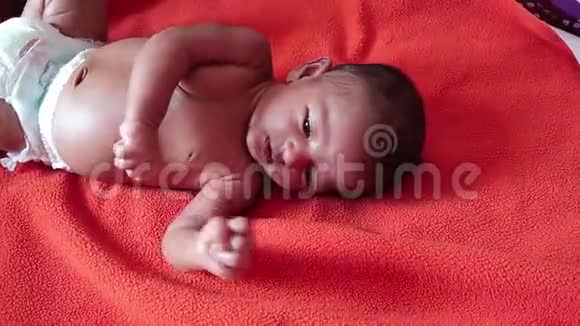 一个婴儿光着身子躺在橙色的红色毛巾表面醒着带着嬉戏的心情睁开眼睛穿着尿布视频的预览图