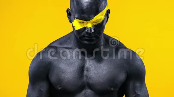 男性健美运动员脸上有黄色的艺术和黑色的身体油漆胸部有肌肉彩色肖像视频的预览图