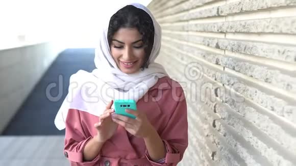 年轻的穆斯林妇女戴着头巾用智能手机发短信视频的预览图