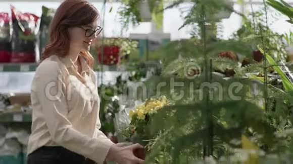 花盆盛开的年轻美丽的微笑女孩的画像温室里绿色植物的背景视频的预览图