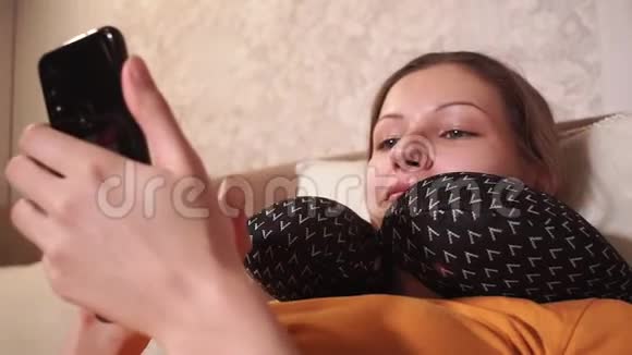 少女正躺在沙发上看着手机浏览着社交网络微笑微笑视频的预览图