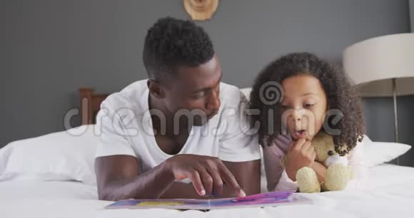 非裔美国父亲在床上给女儿读故事视频的预览图