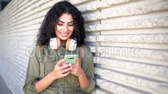 带着耳机的年轻阿拉伯女人在户外使用她的智能手机视频的预览图