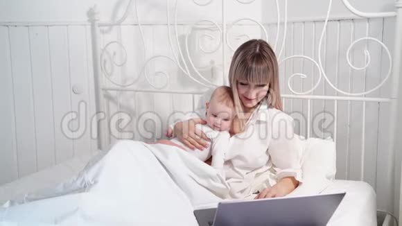 母亲躺在床上婴儿用电脑工作视频的预览图