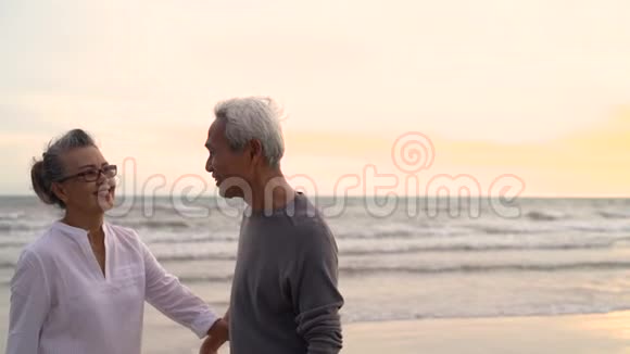 亚洲夫妇老年退休在日落海滩蜜月家庭休息拥抱在一起视频的预览图