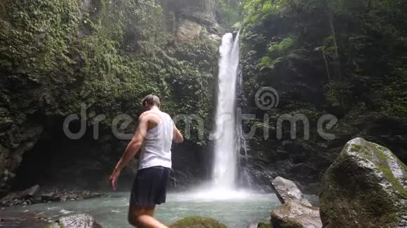 站在瀑布脚下的男游客惊叹于大自然的景色视频的预览图