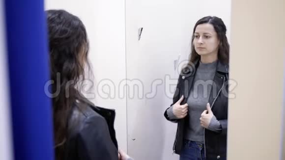 年轻女子试穿皮夹克试衣间服装店视频的预览图