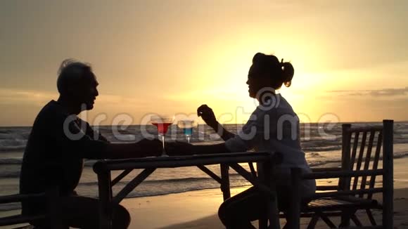 亚洲夫妇年长的长者在日落蜜月时在海滩上放松喝葡萄酒或香槟视频的预览图