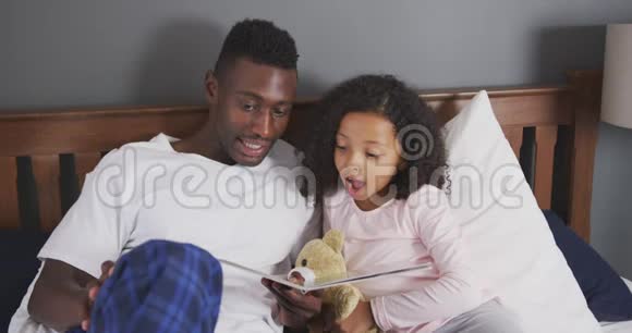 非裔美国父亲在床上给女儿读故事视频的预览图