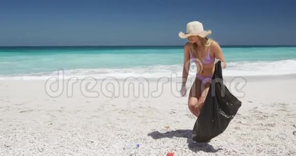女人在海滩上捡垃圾放进垃圾袋视频的预览图