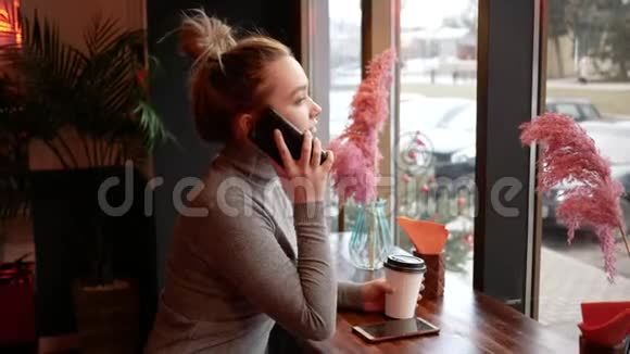 年轻的金发女人在咖啡馆里打电话笑着喝着咖啡视频的预览图