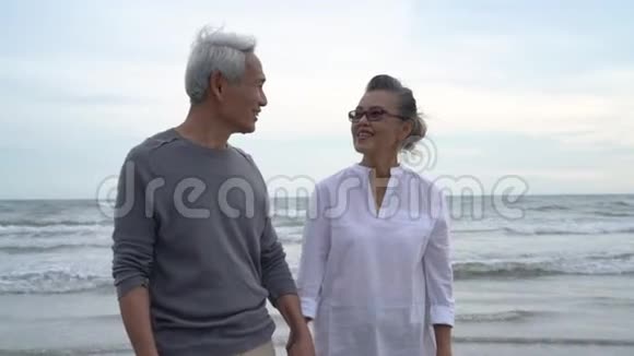 亚洲夫妇年长长者退休后休息放松手牵手散步亲吻日落海滩视频的预览图