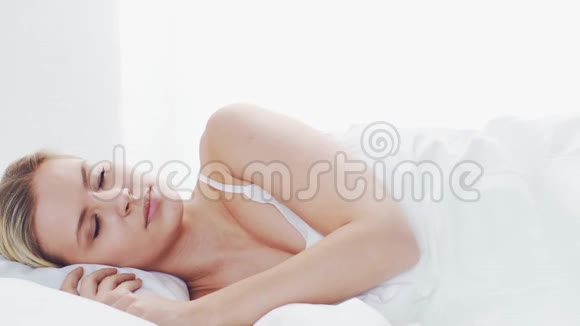躺在床上的年轻女子漂亮的金发睡女孩早上在卧室健康和休息的理念视频的预览图
