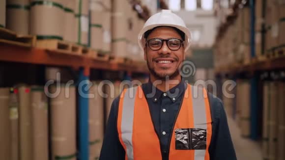 在一个微笑的年轻男性仓库工人或一个站在仓库里的主管交叉双臂时倾斜起来视频的预览图