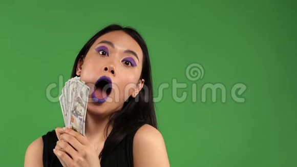 亚洲时髦的年轻女人手里拿着美元背景是孤立的绿色惊喜震惊愉悦的情绪视频的预览图