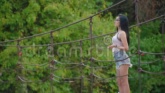 穿短裤的性感黑发女孩站在河边的吊桥上把石头扔进水里视频的预览图