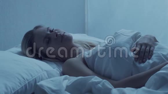 年轻的女人晚上躺在床上美丽的金发女郎卧室里的暮色窗外的月光视频的预览图